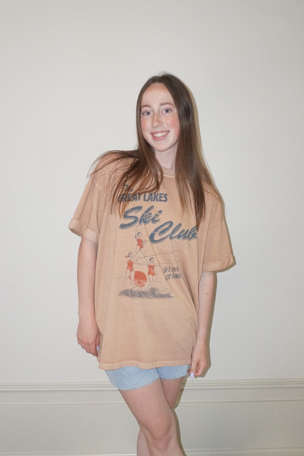 Person wearing a orange t-shirt with water skiing graphics on white wall background