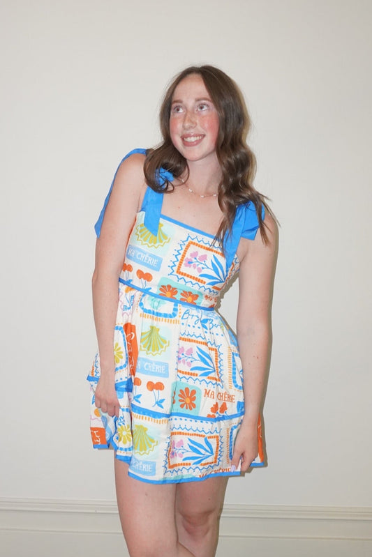 Woman wearing a colorful patterned dress standing against a plain wall.