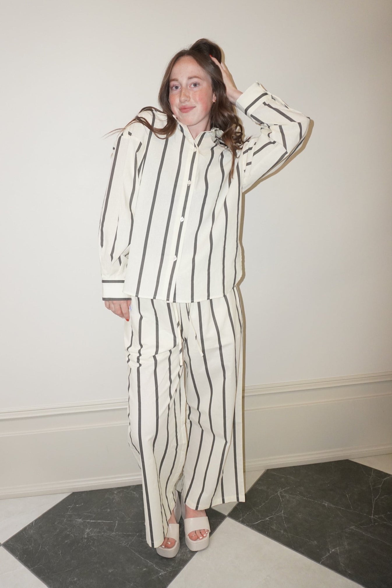 Person wearing a striped pajama set standing against a white wall.