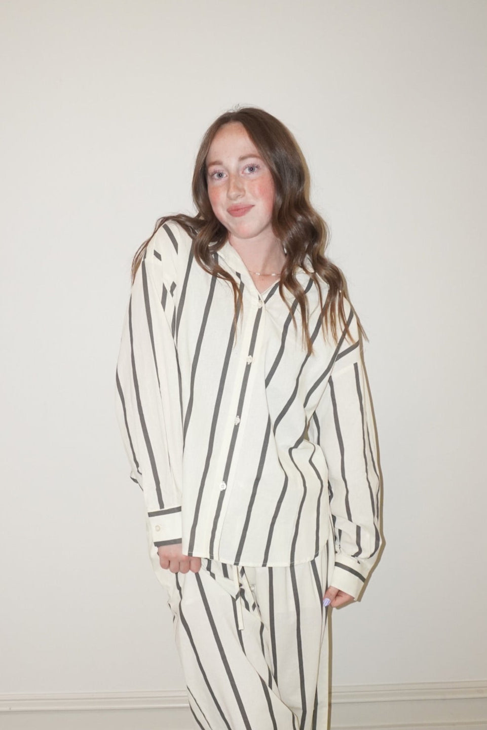 Woman wearing a black and white striped set standing against a plain wall.