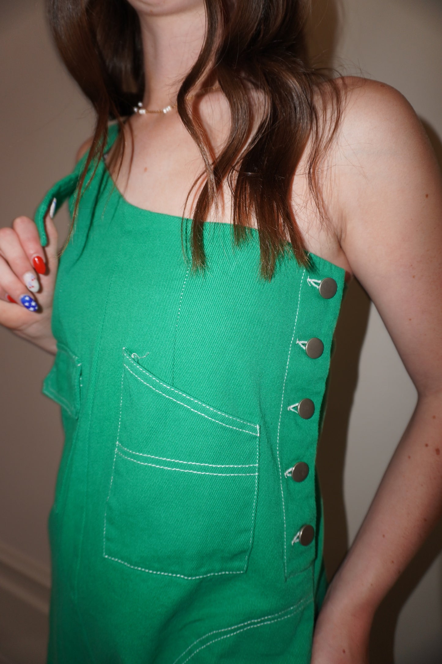 Green romper with button details down the side worn by a person, against a neutral background