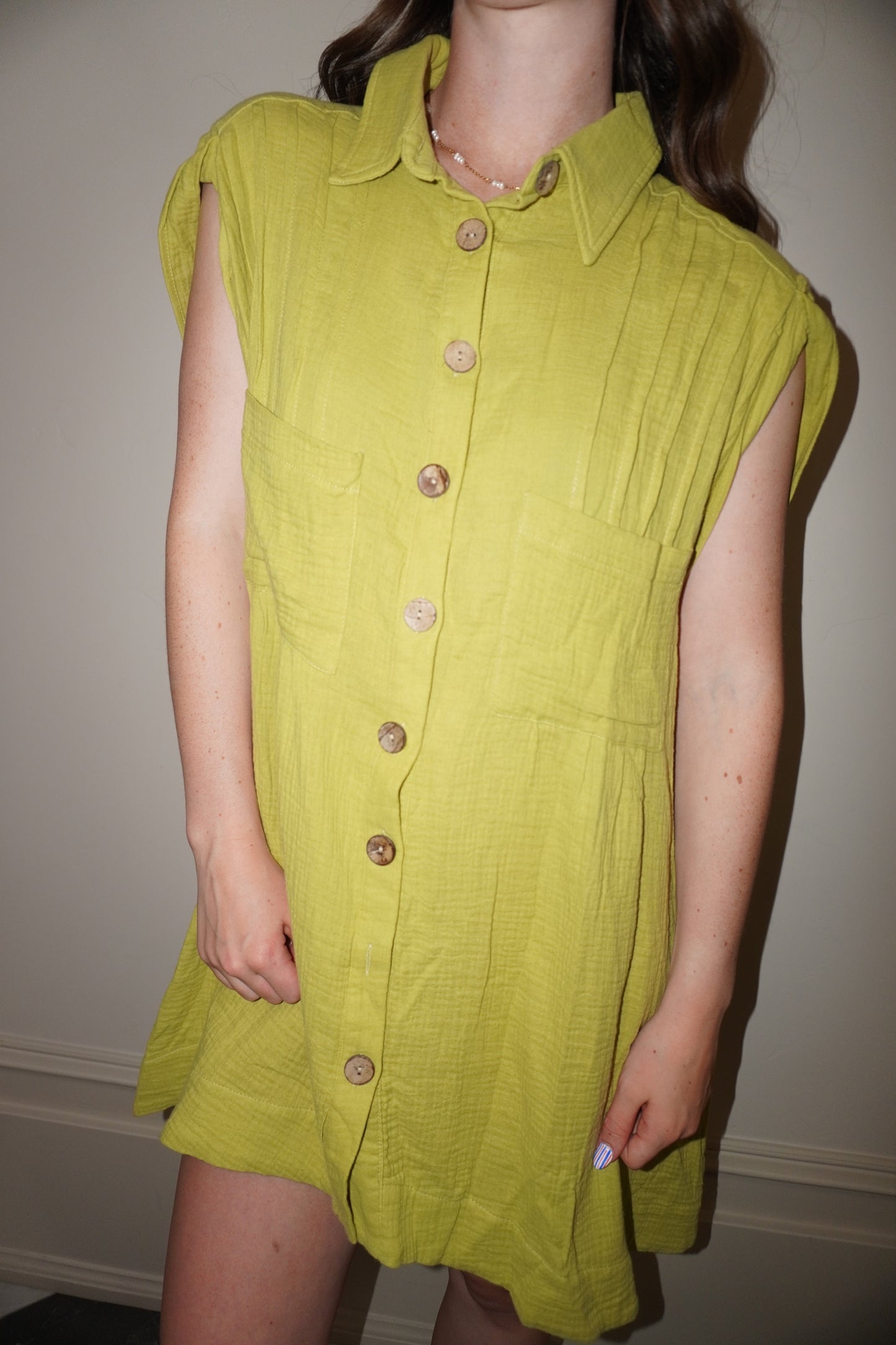 Person wearing a green dress with buttons against a plain background