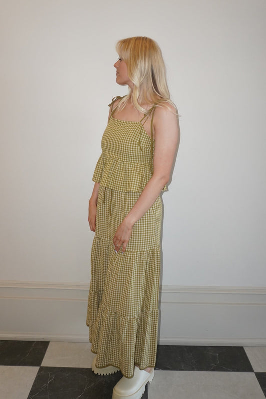 Woman wearing a green checkered set standing against a white wall.