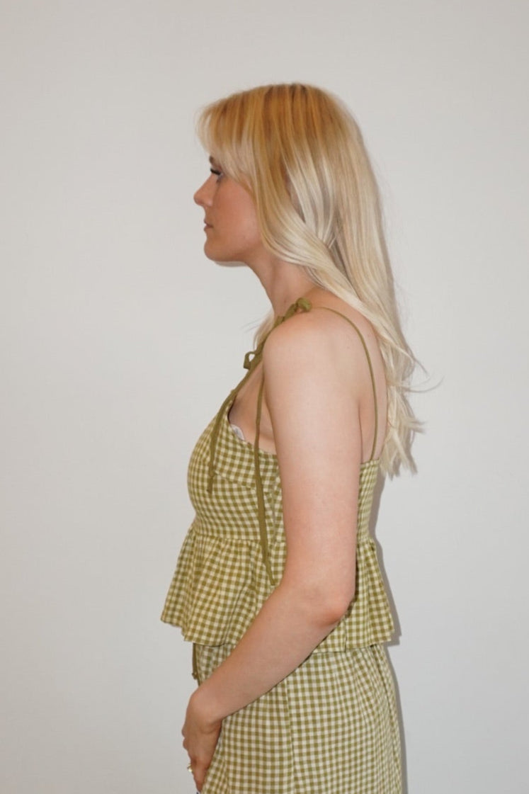 Woman wearing a green checkered set standing against a white wall.