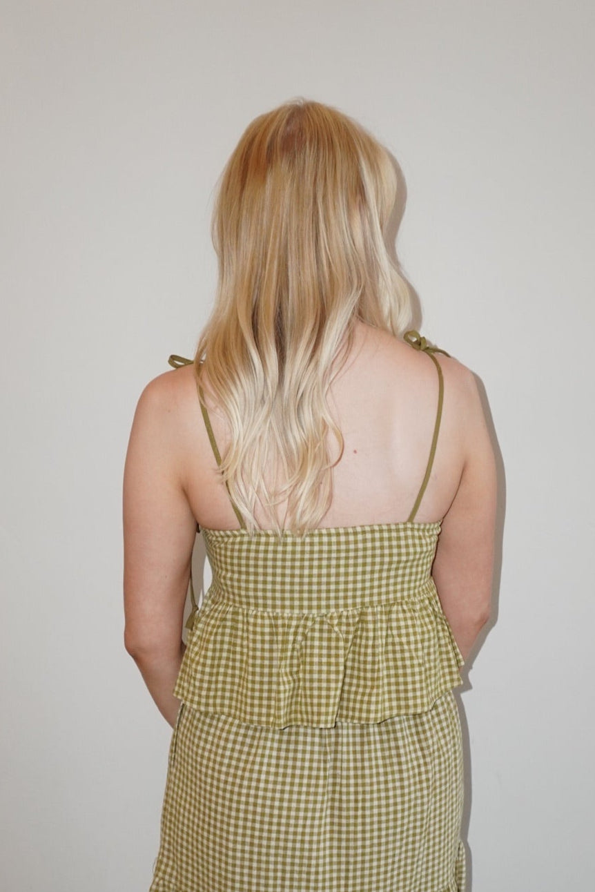 Woman wearing a long, checkered set against a plain wall.