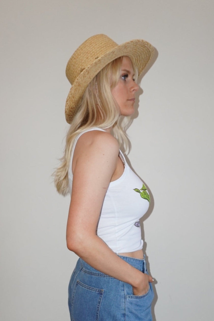 Woman wearing a white top, blue shorts, and a straw hat indoors.
