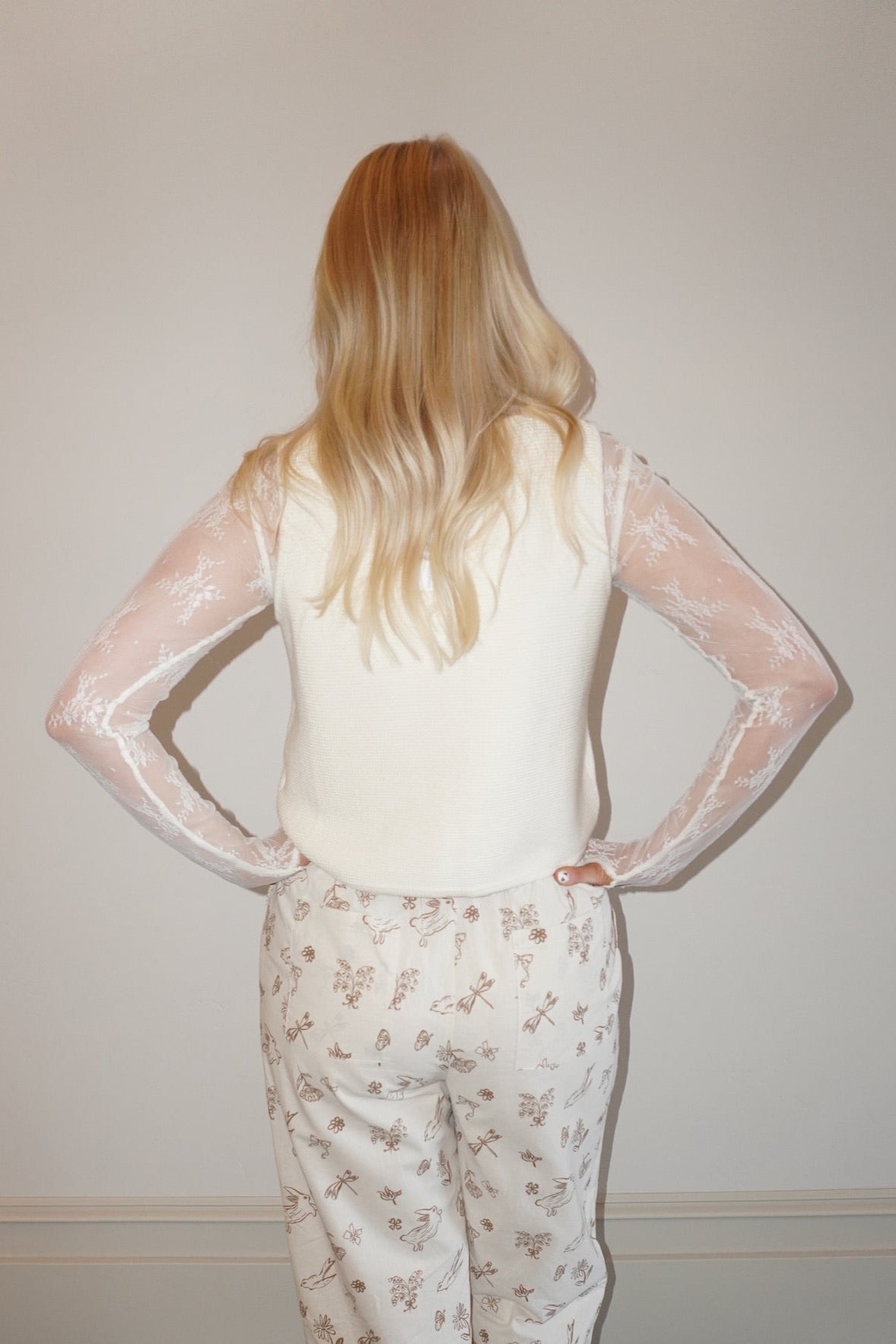 Person wearing a sheer top and floral pants in a room with a checkered floor.