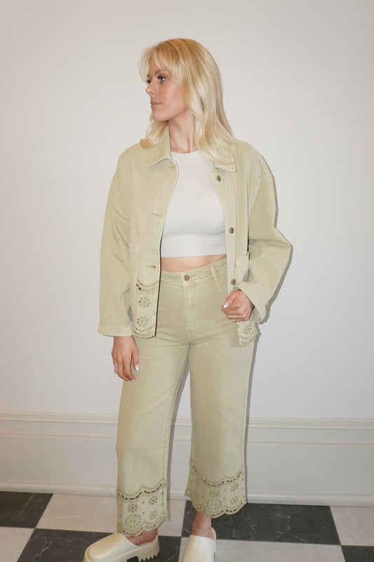 Person wearing a light green jacket and pants with a white top, standing against a plain wall.