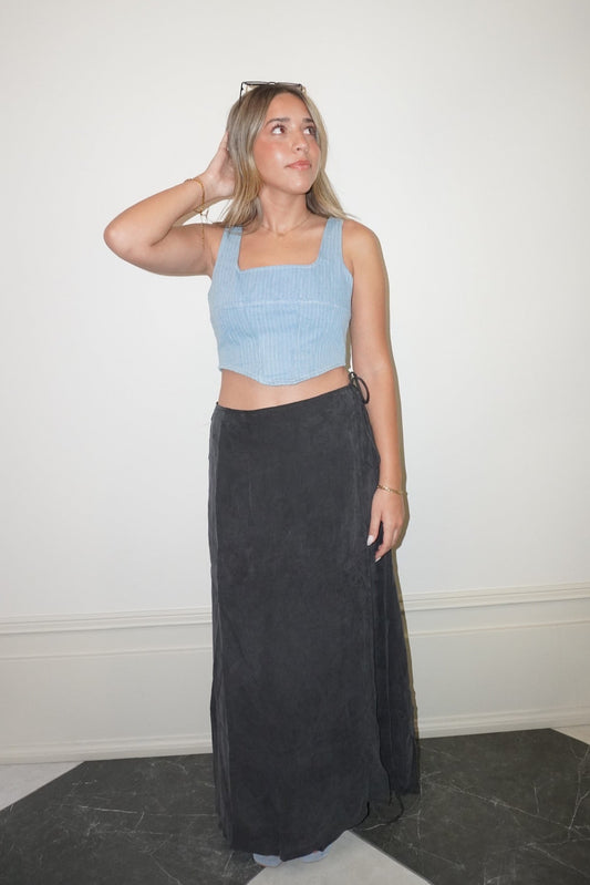 Woman wearing a light blue crop top and dark gray skirt against a white wall.