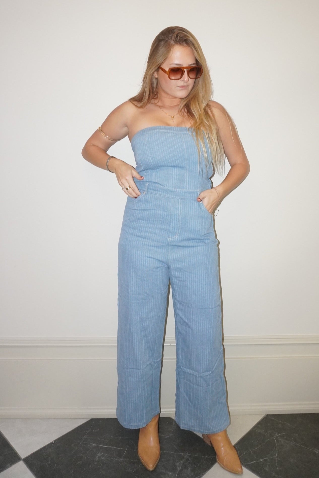 Woman wearing a light blue strapless jumpsuit against a plain wall.