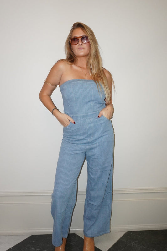 Woman wearing a light blue strapless jumpsuit against a white wall.