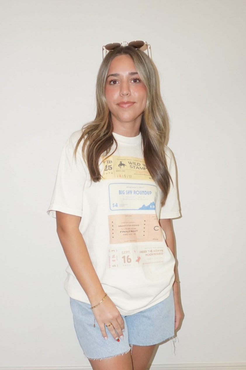 Person wearing a white t-shirt with graphics and denim shorts on a checkered floor.