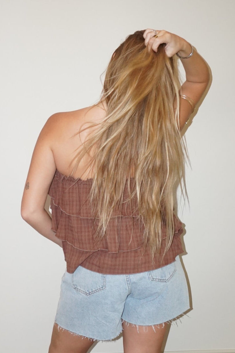 Person wearing a brown top and light blue shorts standing against a white wall.