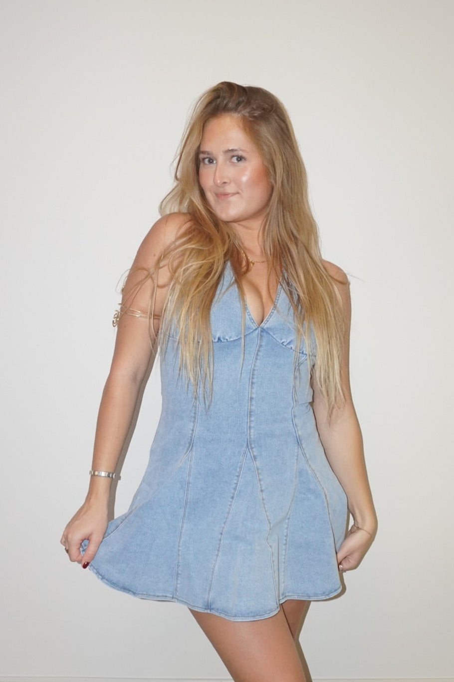 Woman wearing a light blue denim dress standing against a plain wall.