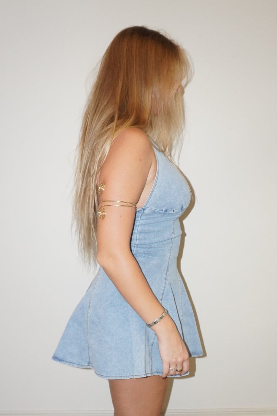 Woman wearing a light blue dress standing against a white wall.