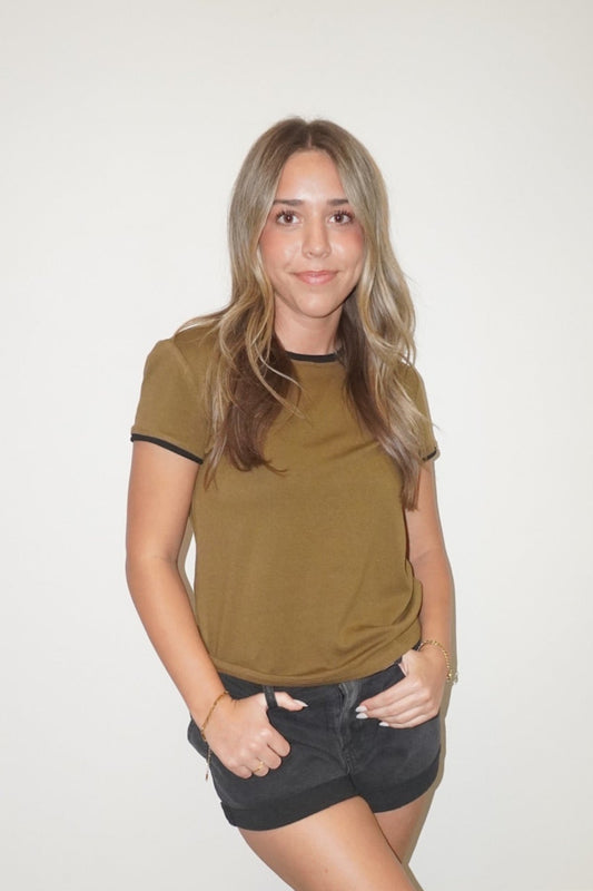 Woman wearing a green t-shirt and black shorts standing against a white wall.