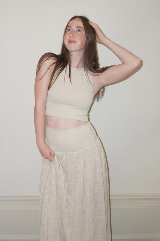Woman in a cream skirt standing in a room with checkered floor and white walls