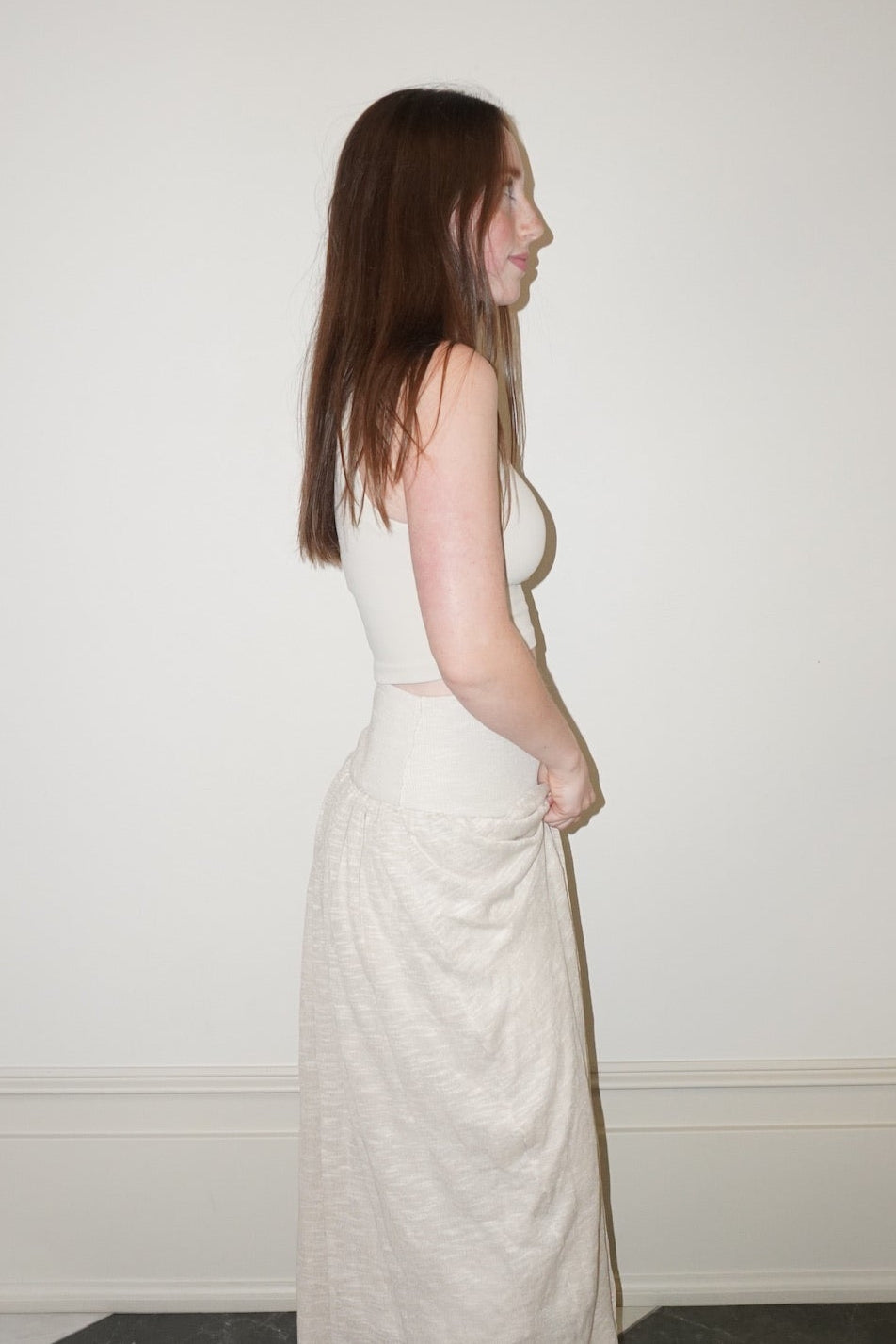 Woman in a cream skirt standing on a checkered floor against a plain wall