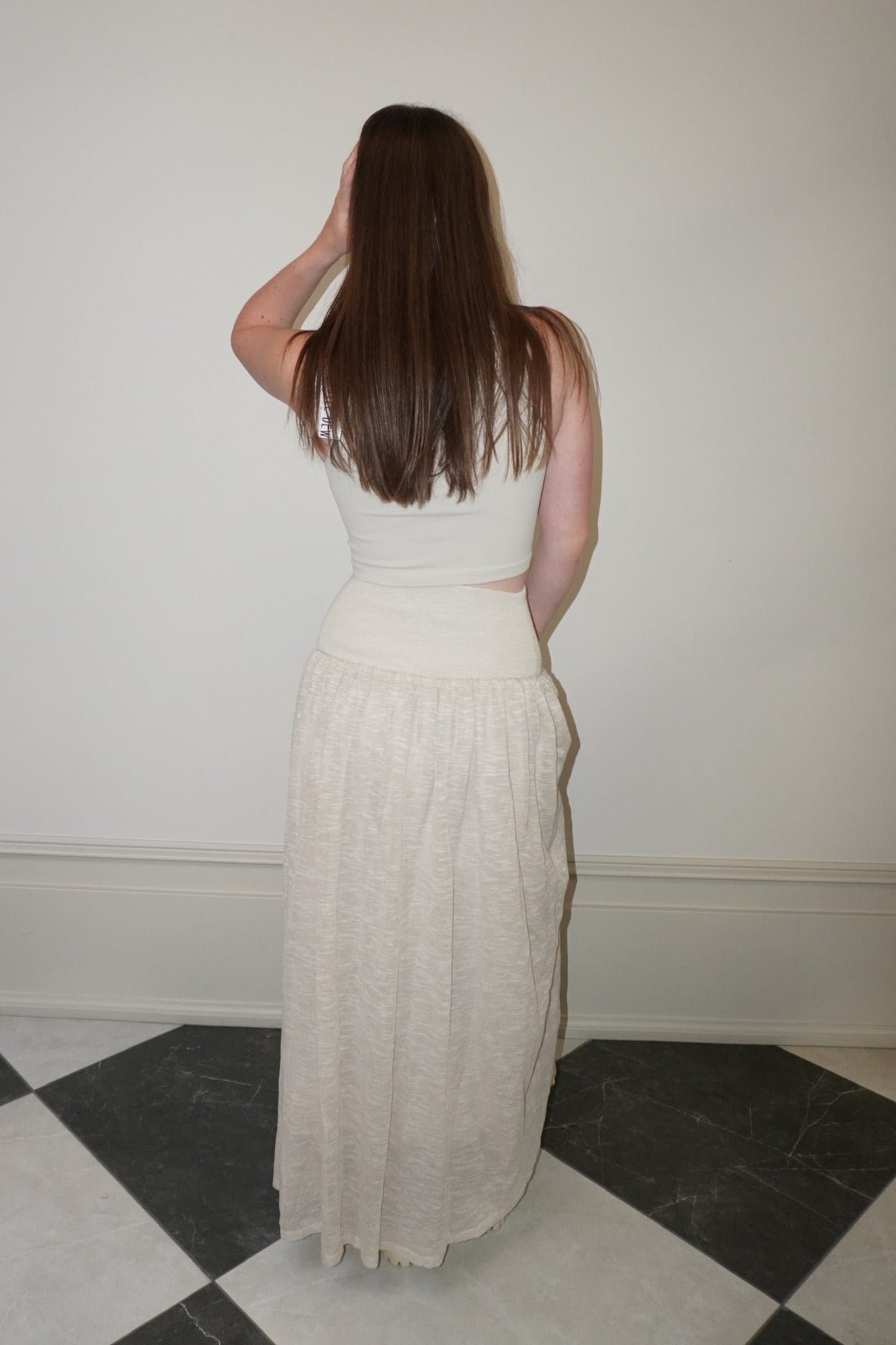 Woman in a cream skirt standing in a room with checkered floor and white walls.