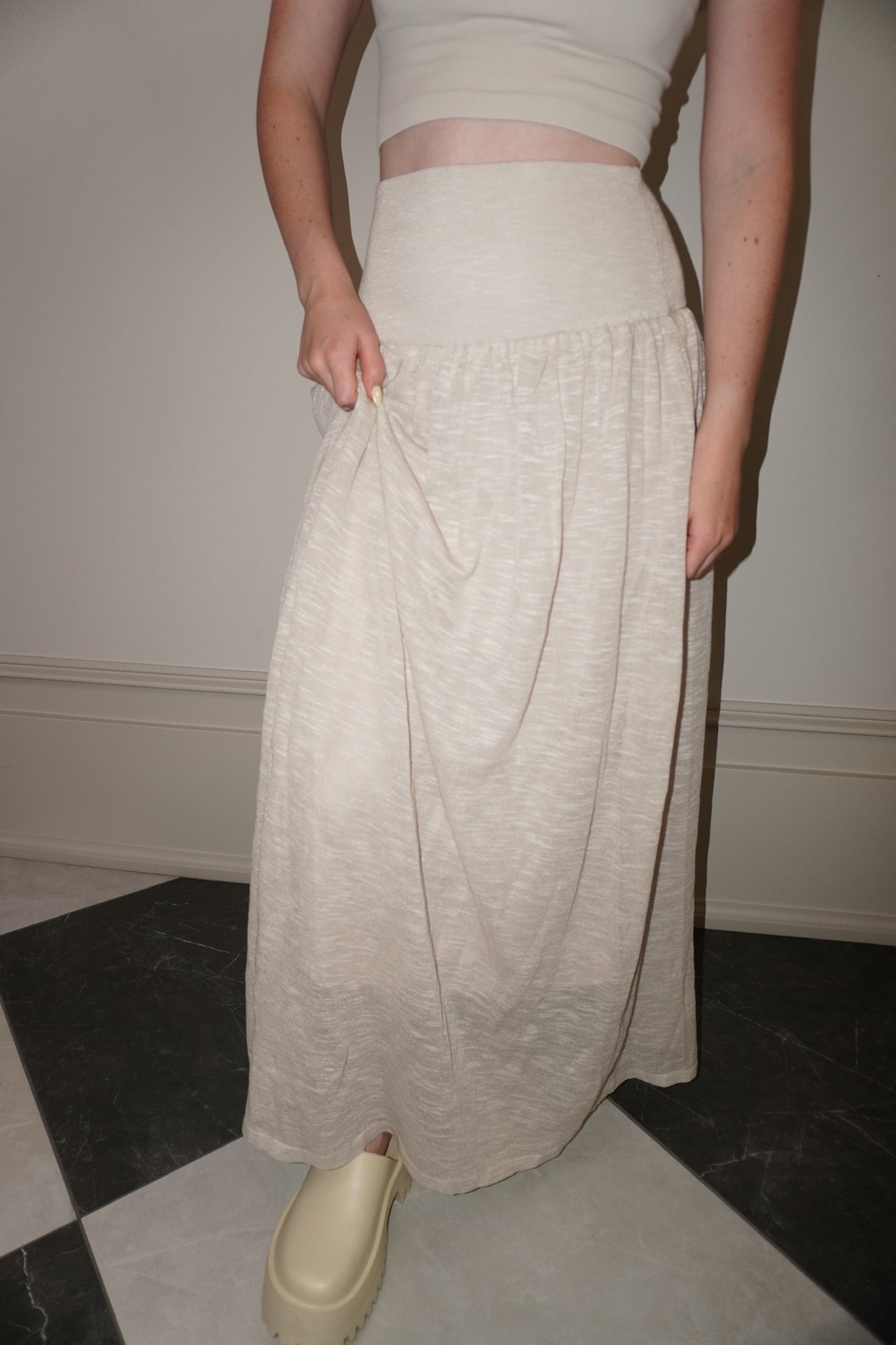 Person wearing a beige skirt and white top in a minimal indoor setting