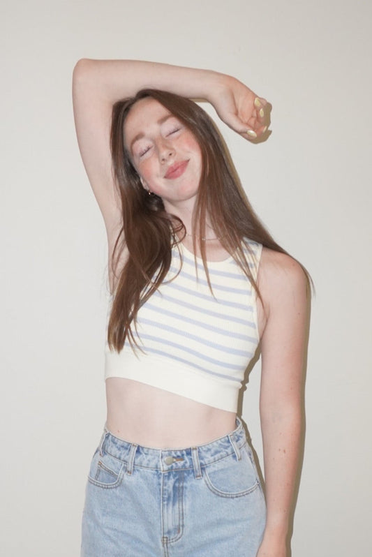 Person wearing a striped tank top and denim shorts standing against a plain wall.