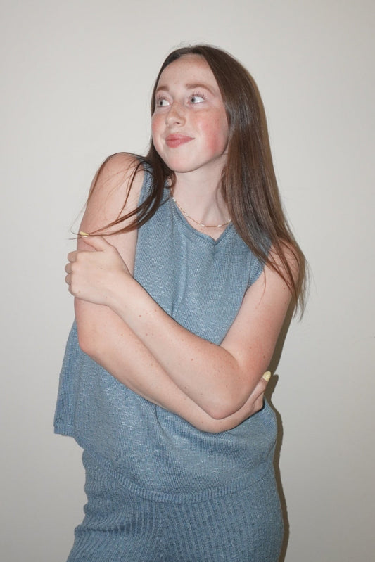 Woman wearing a blue sleeveless top and pants against a plain background