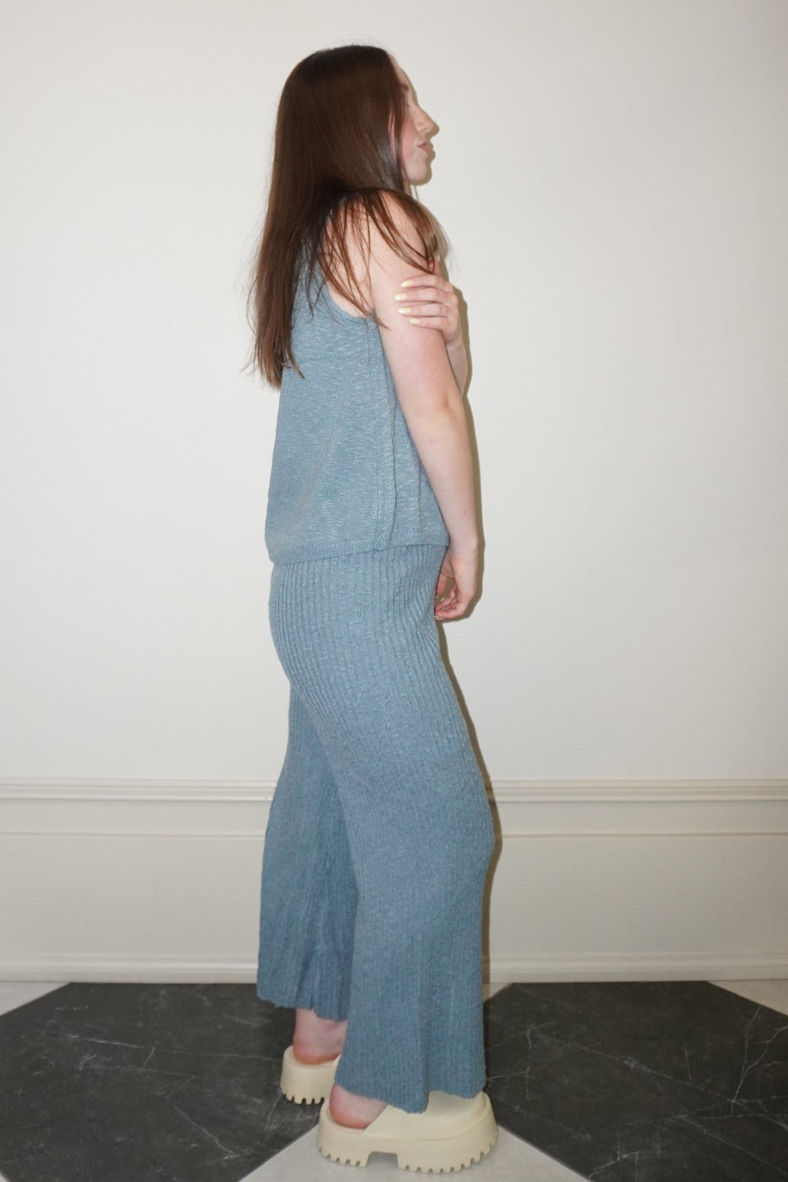 Woman wearing a blue set standing against a white wall.