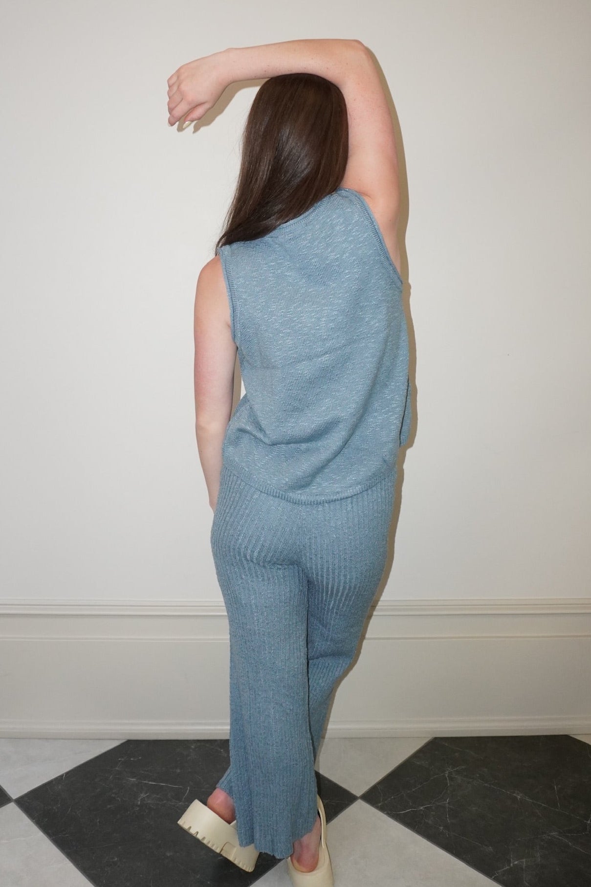 Person wearing a blue sleeveless top and pants standing on a checkered floor.