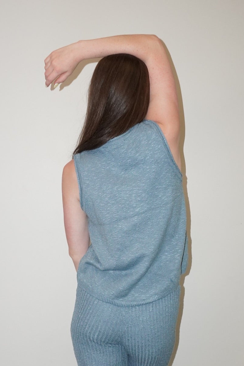 Person wearing a light blue knitted outfit standing against a white wall.