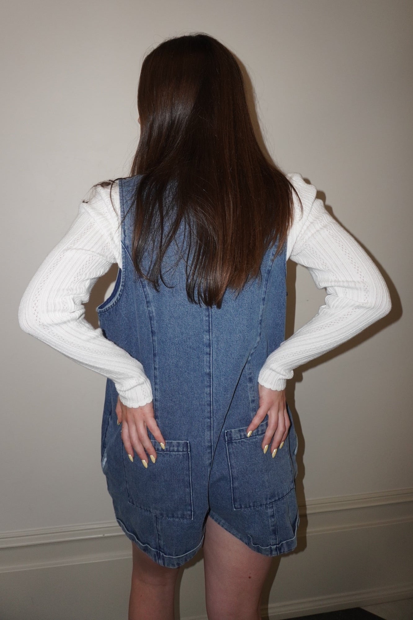 Person wearing a denim overall romper with a plain background