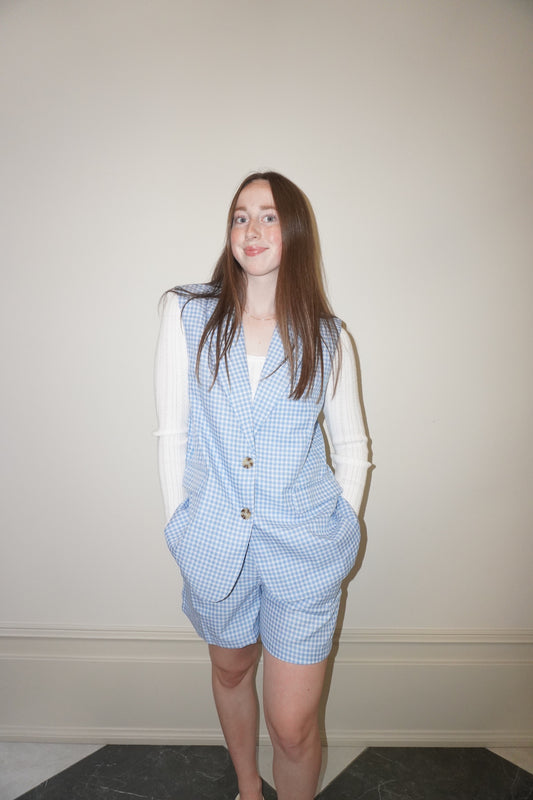 Person wearing a blue checkered vest and shorts against a plain wall.