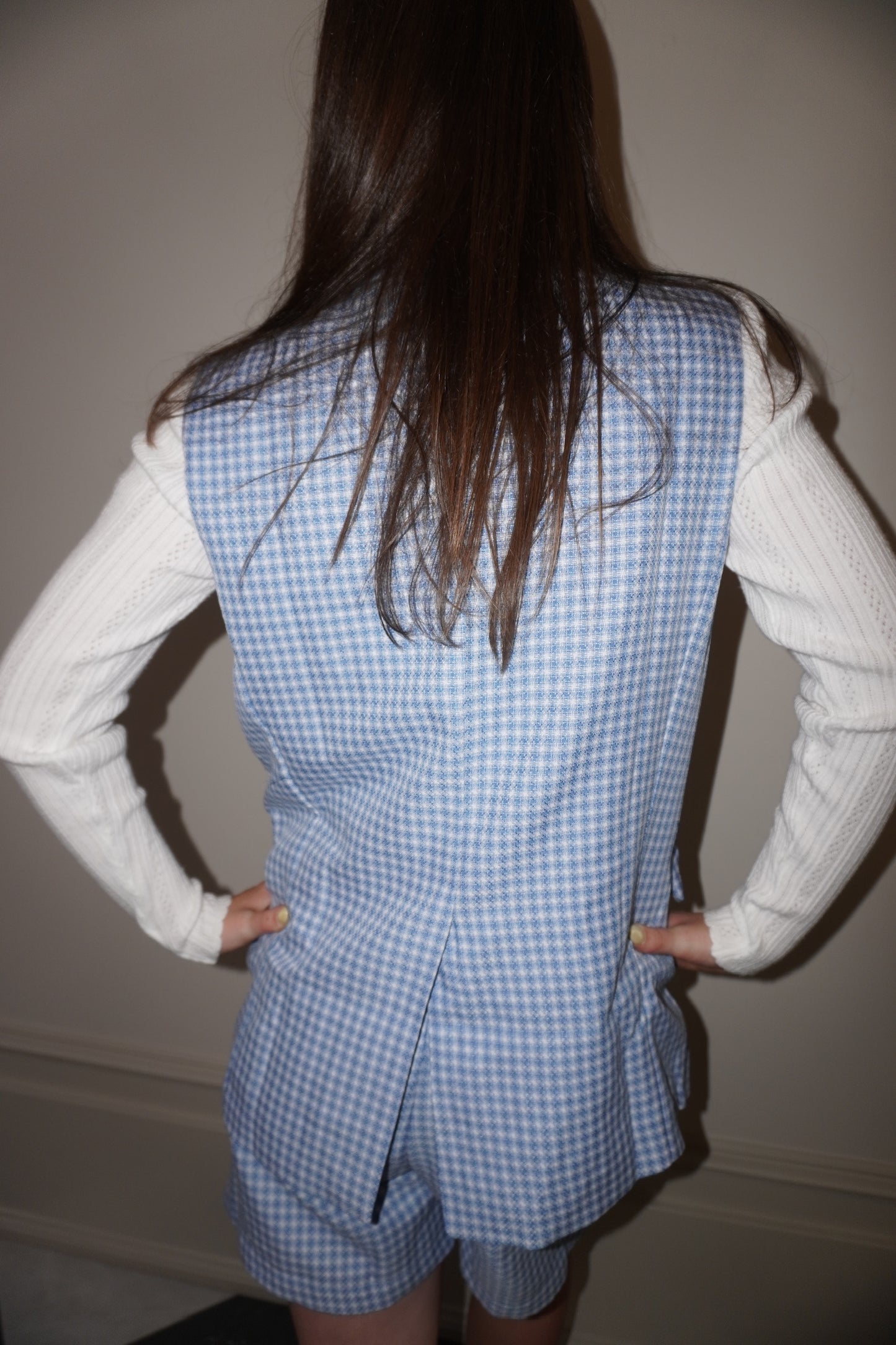 Person wearing a blue checkered set over a white sweater against a plain background