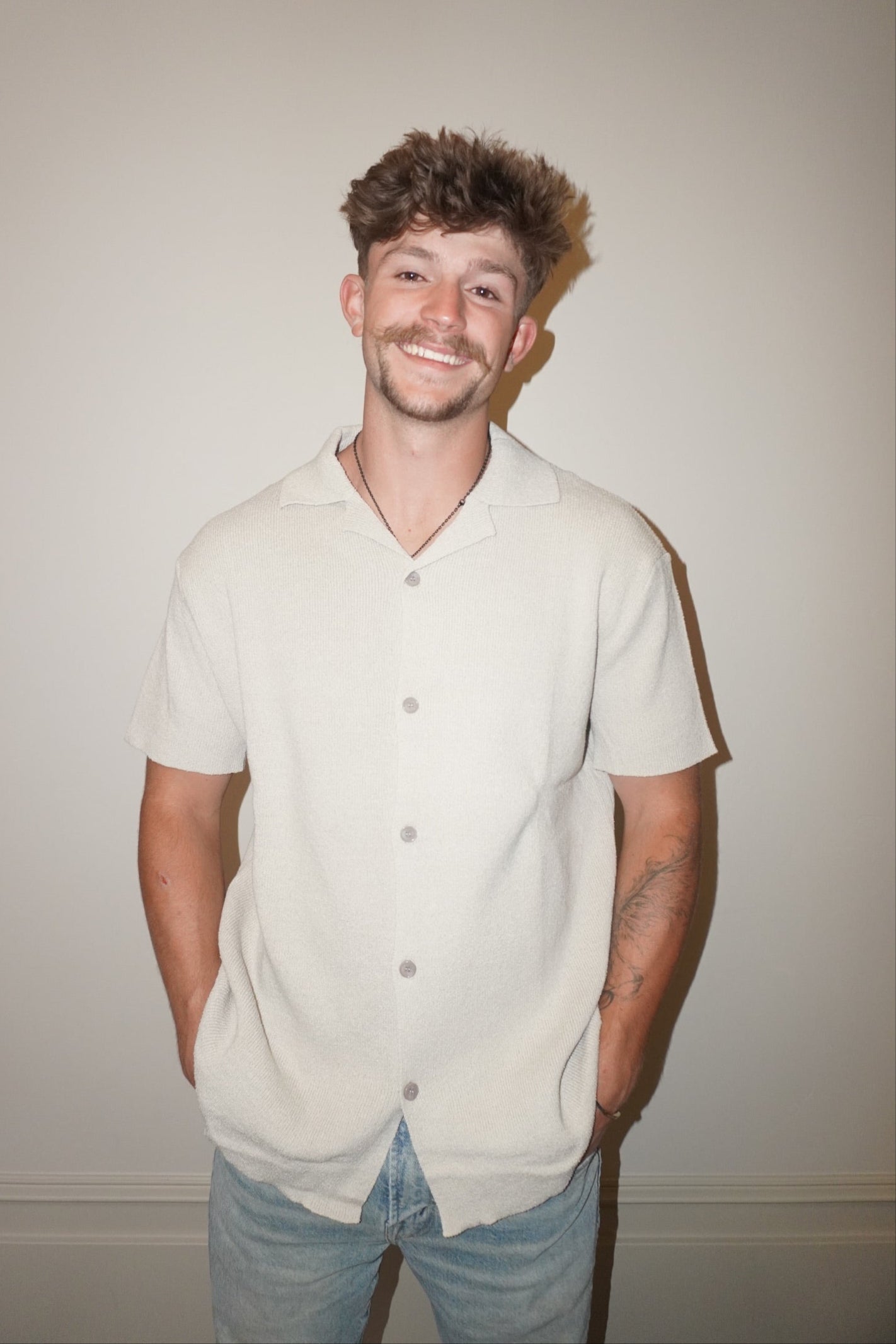 Man wearing a light-colored button-up shirt and jeans against a plain background