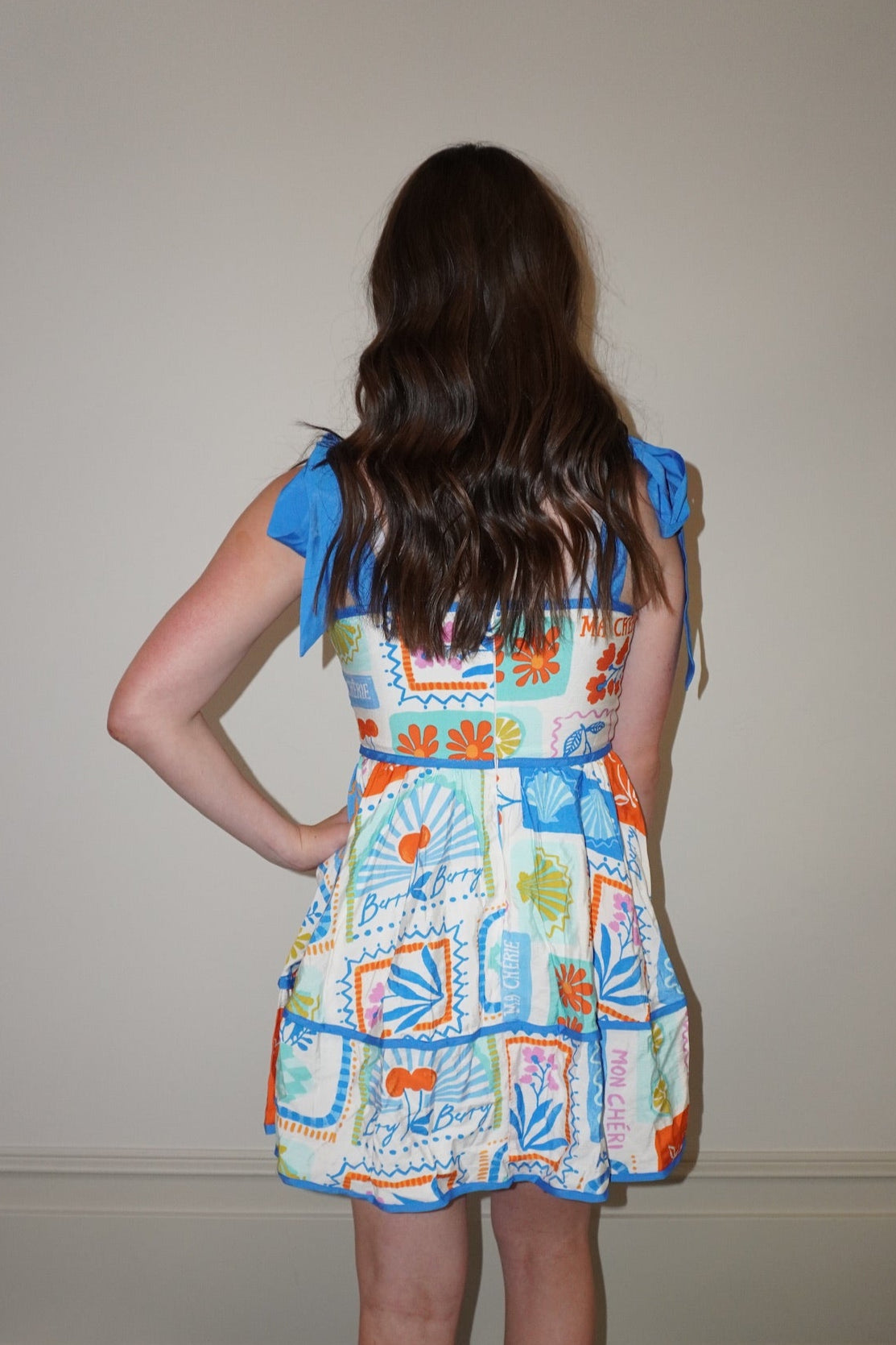 Woman wearing a colorful dress with a pattern of geometric shapes in a room with a checkered floor.