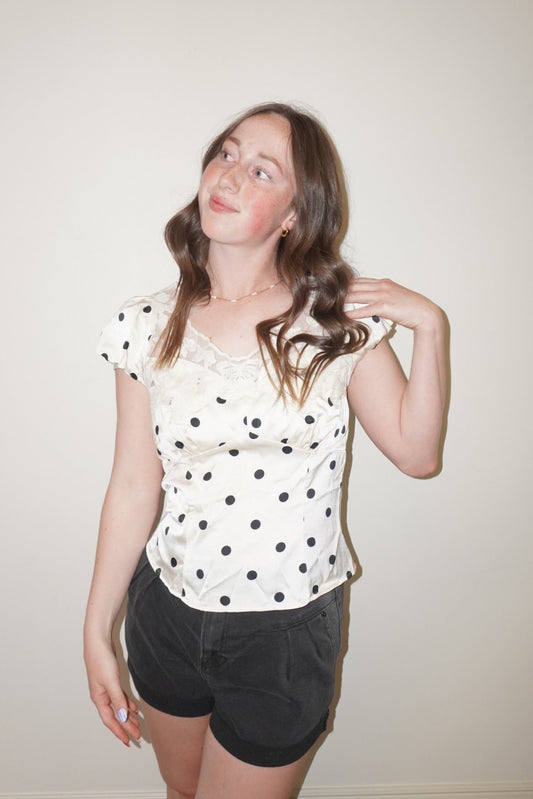Woman wearing a polka dot top and shorts against a plain background
