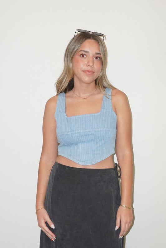 Woman wearing a light blue crop top and black skirt standing against a white wall.
