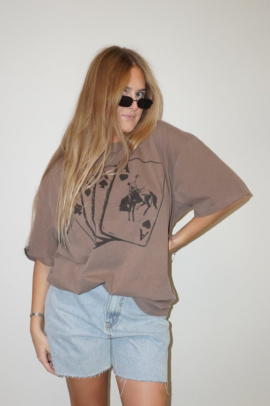 Person wearing a brown oversized t-shirt and light blue shorts against a white wall.