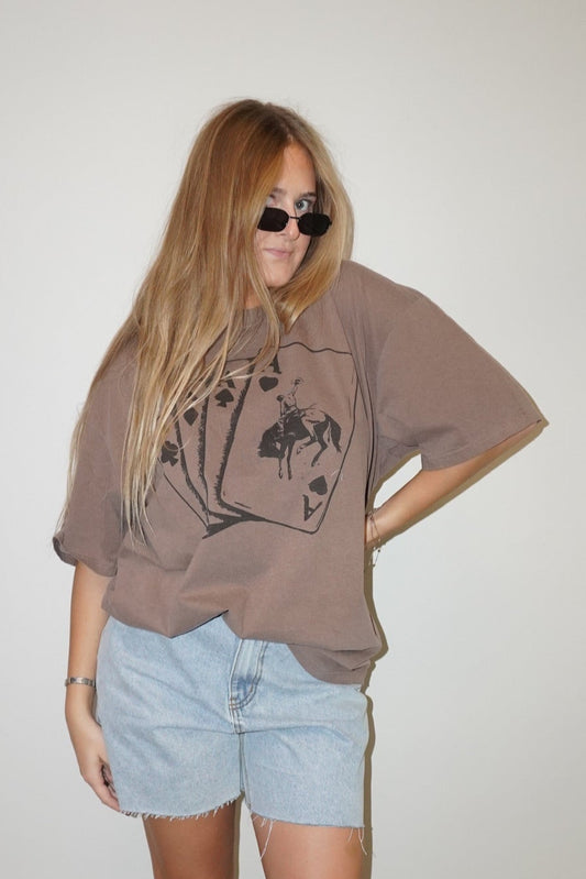 Person wearing a brown oversized t-shirt and light blue shorts against a white wall.