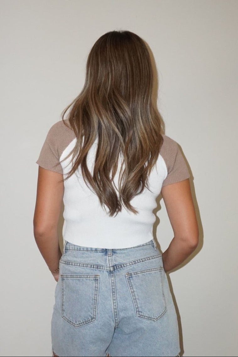 Person wearing a white t-shirt and denim shorts standing against a plain wall.