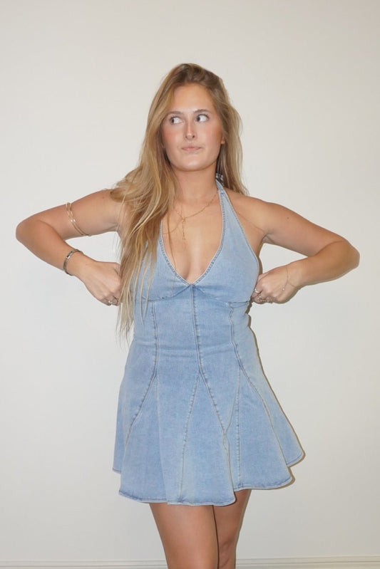 Woman wearing a light blue dress standing against a white wall.