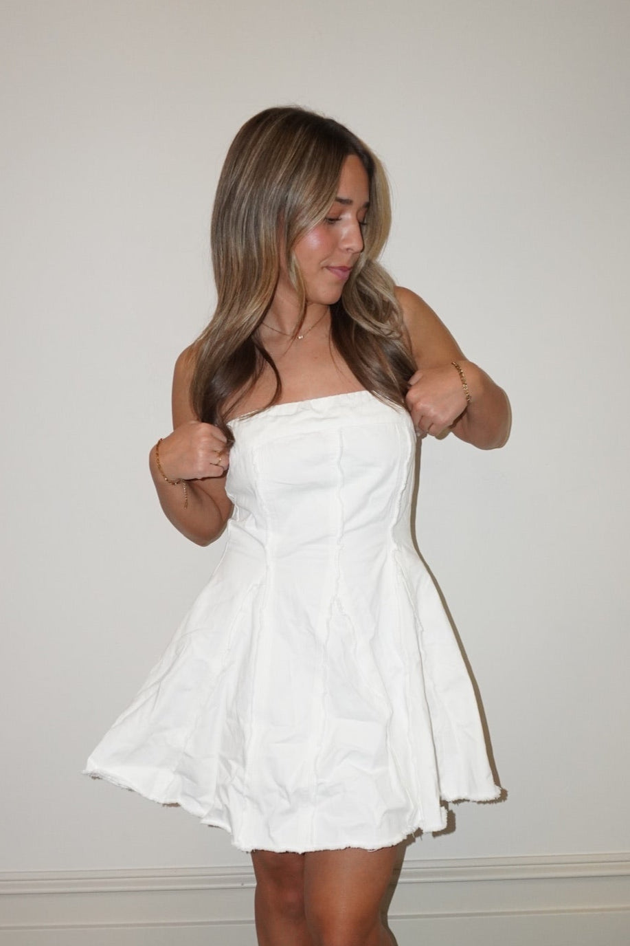 Woman wearing a white strapless dress standing against a plain wall.