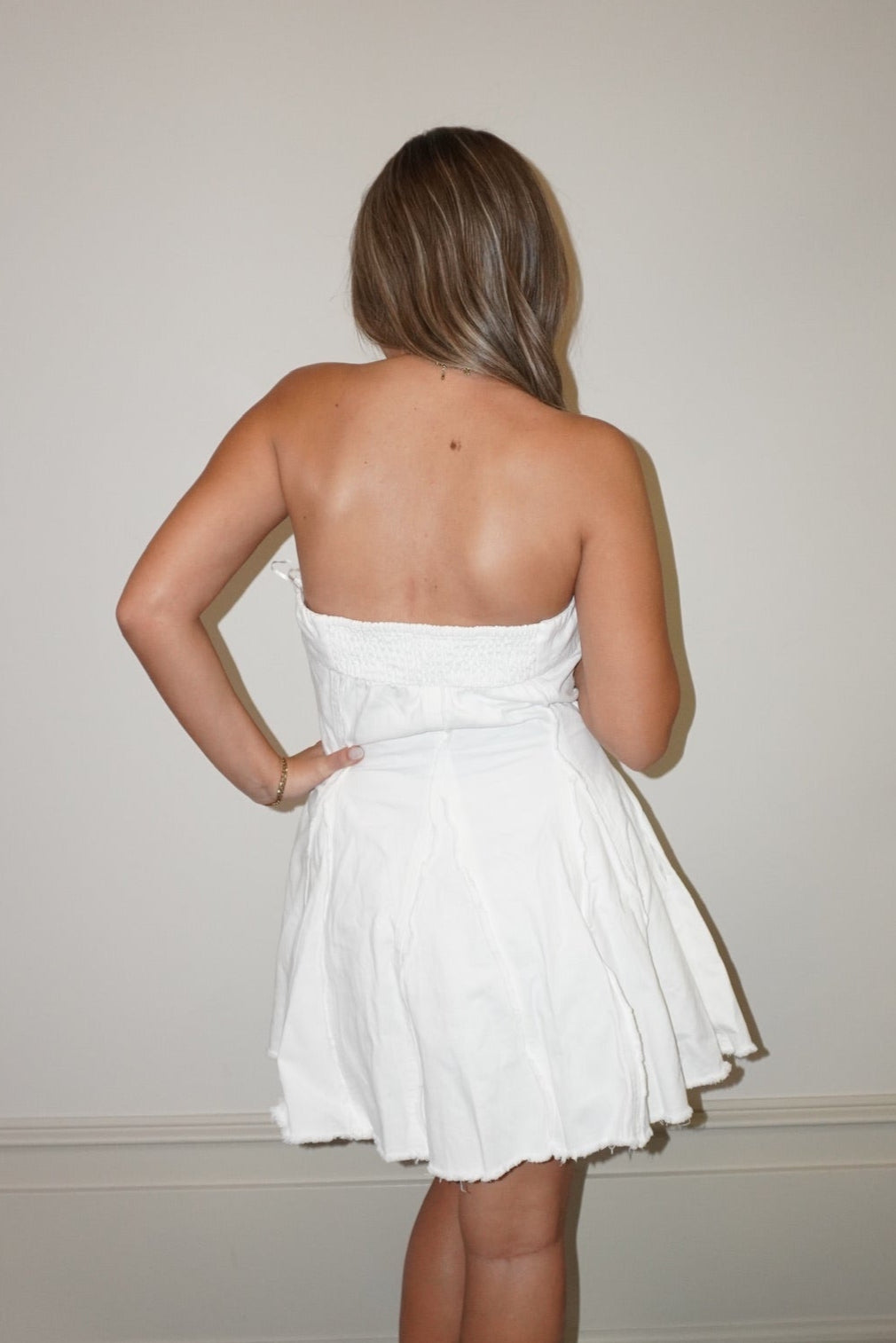 Woman wearing a white strapless dress standing against a plain wall.