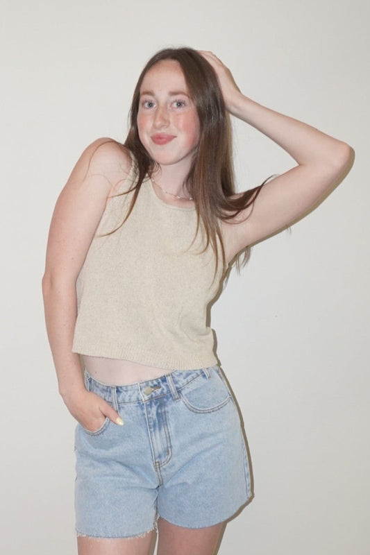 Person wearing a beige sleeveless top and denim shorts standing on a checkered floor.