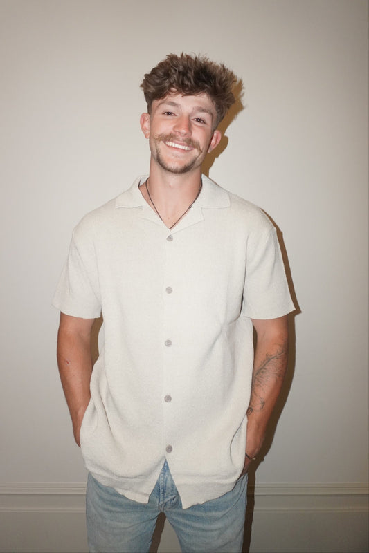 Man wearing a light-colored button-up shirt and jeans against a plain background